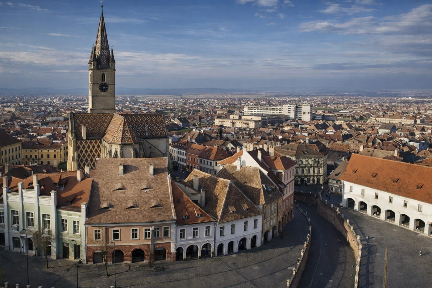 Aerial view of Sibiu's old town, with the Evangelical Cathedral's patterned roof and rooftop dormer windows overlooking the city